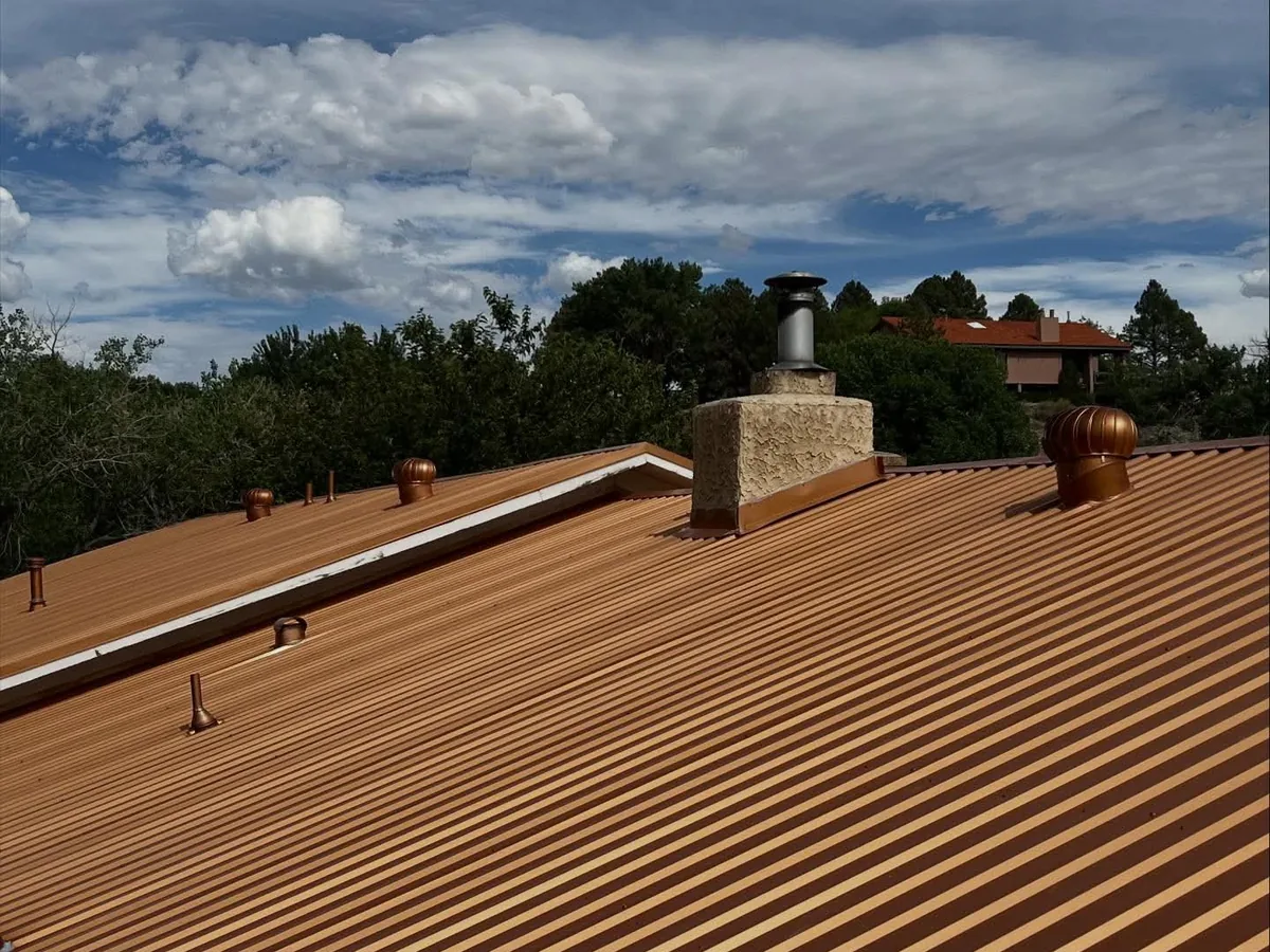 Copper toned metal roof with a chimney and two turbine vents