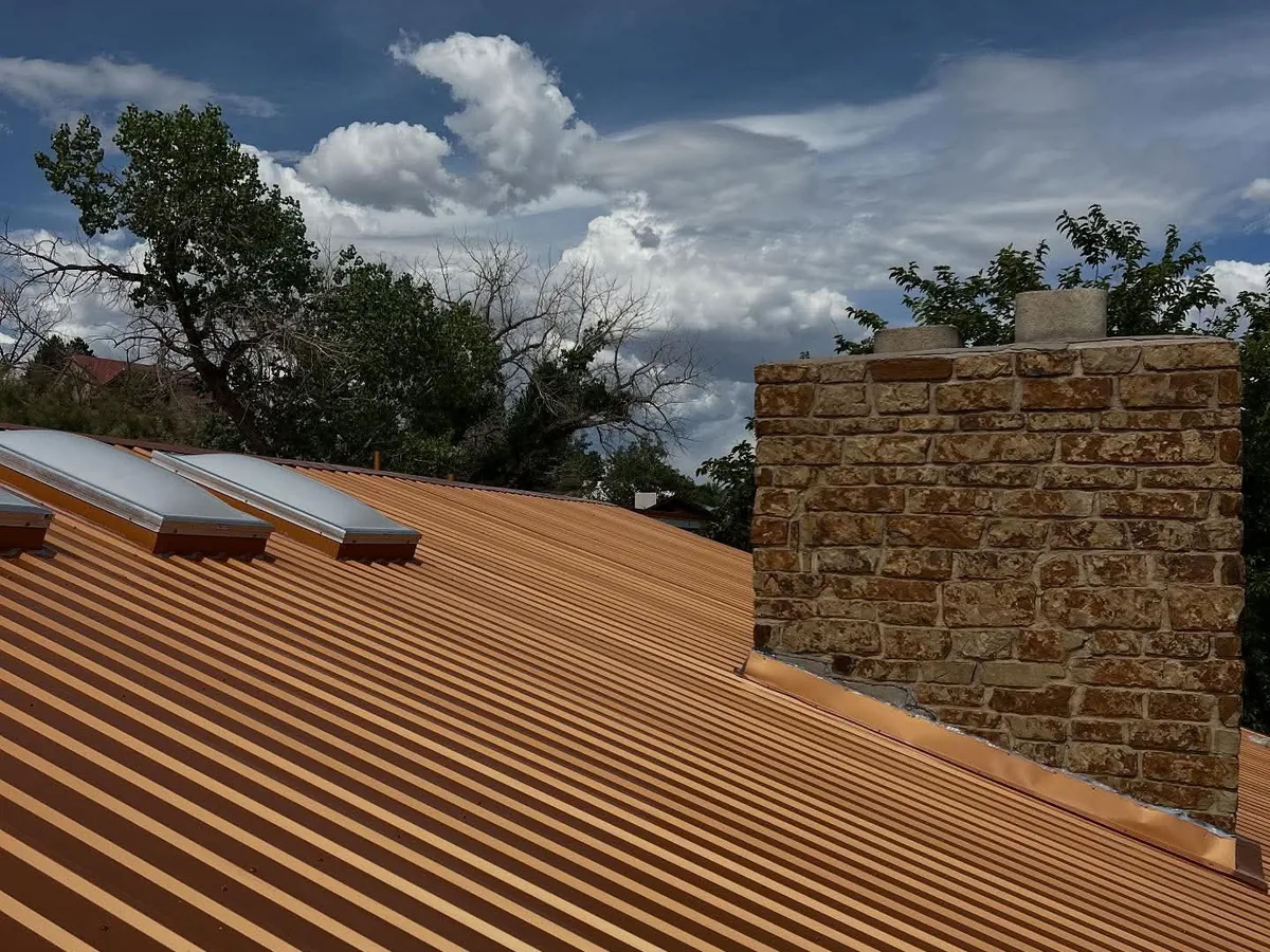 Orange metal roof with skylights and a stone chimney